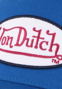 Casquette de baseball bleue avec un patch ovale blanc comportant le texte "Von Dutch" brodé en rouge et une bordure noire. La texture est lisse et le tissu est tissé.