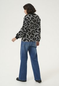 Pullover grigio con stampa leopardata e dettagli neri, vestibilità comoda e maniche lunghe. Un paio di jeans blu a gamba larga con tasche posteriori visibili.