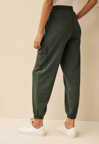 Ciemnozielone spodnie dresowe wykonane z miękkiego materiału, z elastycznym pasem, ściągaczami przy kostkach oraz detalem w postaci bocznej kieszeni.