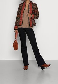 Zwarte en rode gebloemde jas met paisley ontwerp, bruine top, zwarte jeans en bruine hoge laarzen, accessorized met een bruine handtas.