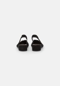 Sandali con tacco in suede nero, aperti sul retro, con una fascia larga sulla volta e una superficie testurizzata. Il tacco spesso offre stabilità.