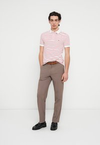 Άσπρο πόλο μπλουζάκι με κόκκινες ρίγες, κοντά μανίκια και γιακά. Συνδυασμένο με μπεζ παντελόνι και μαύρα παπούτσια. Καφέ ζώνη προσθέτει λεπτομέρεια.