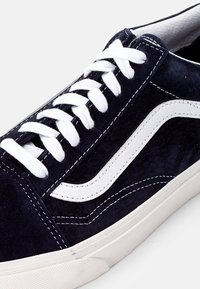 Baskets en suède bleu marine avec une bande latérale en cuir blanc. Elles présentent des lacets blancs, des coutures contrastantes et une semelle en caoutchouc texturée.