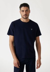 Marineblå bomulds T-shirt med rund halsudskæring, korte ærmer og en lille trekantet logoaccent på venstre bryst.