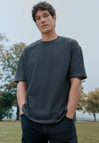 Donkergrijze T-shirt met korte mouwen en ronde hals, ontspannen pasvorm, van katoen met zichtbare stiksels, gecombineerd met donkere jeans.