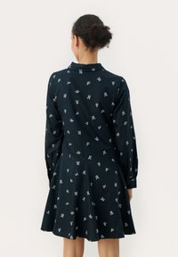 Robe marine à manches longues, col boutonné et jupe évasée, présentant un motif floral blanc et un tissu texturé.