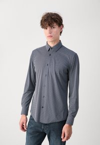 Srajca z dolgimi rokavi, ki ima modro-bele pike, ovratnik in modre gumbe, izdelana iz gladkega materiala.
