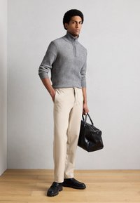 Maglione grigio a coste con collo alto, pantaloni color crema e borsa in pelle nera. Le scarpe sono nere con suola spessa.