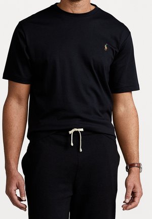 Camiseta negra de algodón con cuello redondo y mangas cortas, con un pequeño logo bordado en el pecho izquierdo. Combinada con pantalones negros a juego.