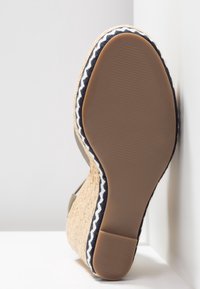 Semelle compensée en espadrille avec détails en jute texturé, accent en tissu bleu foncé, et partie inférieure en caoutchouc avec un motif côtelé.
