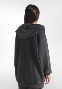 Felpa nera over-size in tessuto texturizzato, con cappuccio grande e polsini a coste. La parte posteriore ha una finitura liscia e un taglio morbido.