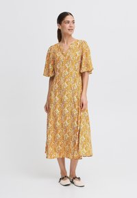 Rochie midi galbenă cu imprimeu floral, cu mâneci scurte tip flutură și decolteu în V, având un model paisley și un material fluid.