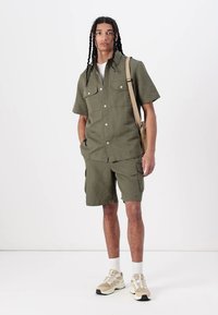 Chemise à manches courtes vert olive avec deux poches poitrine, accompagnée de shorts cargo assortis. Présente une coupe décontractée et est fabriquée à partir de matériau léger.