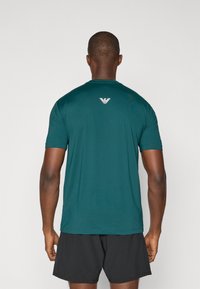 T-shirt atlético em turquesa feito de tecido leve, com mangas curtas e decote arredondado, apresenta um pequeno logo branco na parte superior das costas.