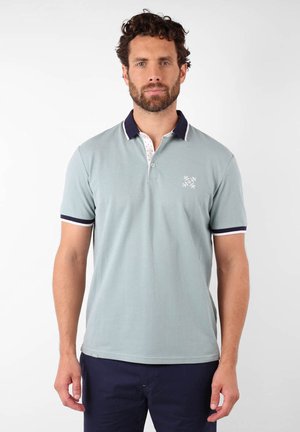 Polo en vert clair avec un col marine et des accents blancs. Doté de manches courtes et d'un petit logo sur la poitrine. Texture lisse.