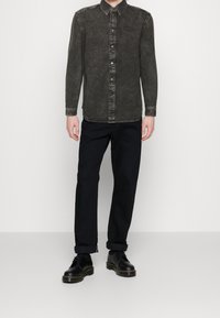 Mörkgrå denimskjorta med knapplås, klassisk krage och kontrastsömmar. Kombinerad med svarta byxor och svarta skor.