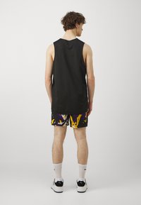 Camiseta sin mangas negra combinada con pantalones cortos de patrón abstracto colorido en púrpura, amarillo y negro. El calzado es negro y blanco.