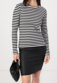 T-shirt à rayures à manches longues en tissu côtelé noir et blanc, associé à une mini jupe en cuir noire ajustée et à une pochette noire texturée.