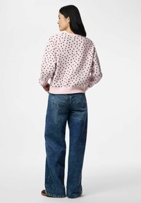 Sweat-shirt rose clair à pois foncés, avec poignets et ourlet côtelés, associé à un jean en denim bleu taille haute, affichant une coupe décontractée.