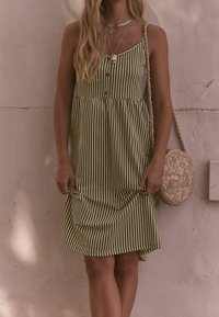 Grün-weiß gestreiftes Kleid mit tailliertem Oberteil, Knopfdetails und schwingendem Rock. Kombiniert mit einer Tasche mit geflochtenem Riemen.