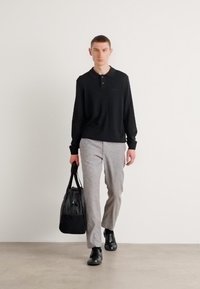 Črn polo s dolgimi rokavi, svetlo sivi hlače, črne usnjene čevlje in črna torba. Gladek material, sproščen kroj, minimalističen dizajn.
