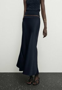 Jupe maxi bleu marine en tissu doux et fluide avec un design évasé. Le modèle l'associe à un haut en tricot et des sandales noires.