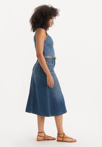 Denim to-deltakostyme som består av en tettsittende blå denim crop top og et flared midi-skjørt. Stoffet har en klassisk denim tekstur og farge.