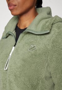 Fleece jack in lichtgroen, met een ritsluiting, hoge kraag, gestructureerd oppervlak en een decoratieve logo op de borst.