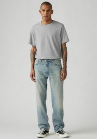 Camiseta de algodón gris combinada con jeans de mezclilla de pierna recta en azul claro. El conjunto se complementa con zapatillas de lona en blanco y negro.