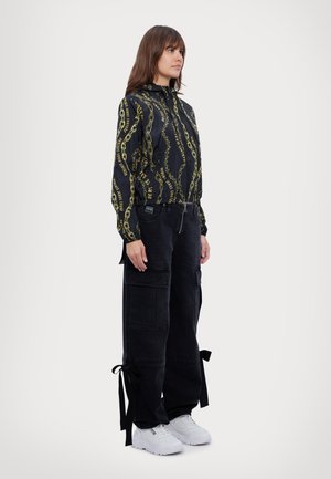 Black patterned jacket with yellow chains; black cargo pants with pockets and tie accents; white sneakers. Simple and functional design.