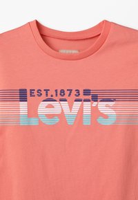 Koralowa bawełniana koszulka z okrągłym dekoltem i poziomym wzorem w paski w kolorze niebieskim i białym z napisem "Levi's" oraz "EST. 1873".