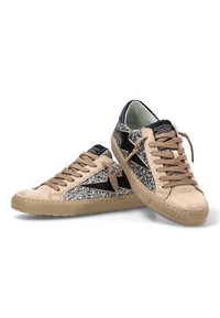 Zapatillas beige con lados plateados brillantes, diseño de estrella negra, cordones beige y suelas de goma beige, posicionadas cruzadas sobre un fondo blanco.