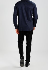 Námořnický modrý vzorovaný dlouhý rukáv s rovním lemem, kombinovaný s černými kalhotami a lesklými černými botami. Jednoduché pozadí.