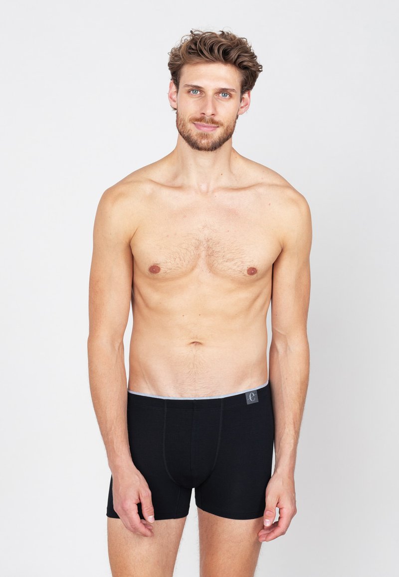 Zwarte boxer shorts met een grijze tailleband en logo. De stof lijkt soepel en rekbaar, en past snugly rond de taille en benen.