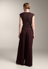 Burgundy tvådelad outfit med en figurnära topp med korta ärmar och vida byxor, tillverkad av ett mjukt tyg, med rena linjer och utan synliga mönster.