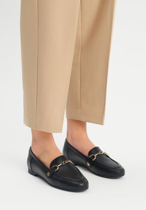 Zwarte leren instappers met een ronde neus, voorzien van een gouden kettingdetail en een klassiek ontwerp. Draag ze met beige recht gesneden broek.