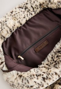 Intérieur de sac en fausse fourrure marron clair avec une bordure imprimée léopard. Comprend une poche zippée marron et un patch logo avec le nom de la marque "NEXT".