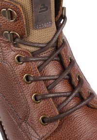 Bota de cuero marrón con superficie texturizada, ojales de latón y cordones marrones. La parte superior incluye un panel de tela color beige, lo que mejora su durabilidad.