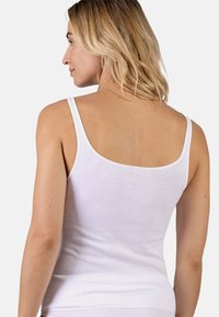 White tank top with thin straps. Soft, smooth cotton material. Fitted design, minimal seams, with a plain texture and no visible patterns.