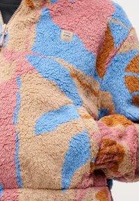 Πολύχρωμο φλις μπουφάν με ροζ, μπλε, καφέ και καμηλό αφηρημένα μπαλώματα, κλείσιμο  με φερμουάρ και μικρό ορθογώνιο λογότυπο στο στήθος.