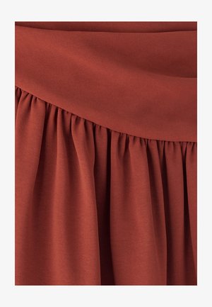 Tkanina boje hrđe s glatkom teksturom i naboranim dizajnom u struku, stvarajući tekući i mekani izgled.