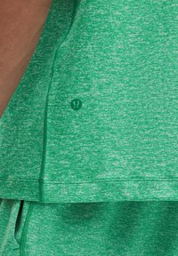 Grünes Sportoberteil aus strukturiertem, meliertem Stoff. Verfügt über glatte Nähte und ein kleines Logo-Element in passender Farbe.