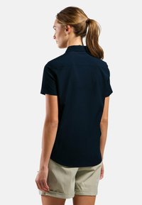 Navy short-sleeved shirt with a collar and button detail at the back, paired with light-colored shorts. Smooth fabric and relaxed fit.
