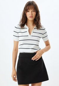 Witte geribde polo met marineblauwe strepen, korte mouwen en een V-hals. Gecombineerd met een zwarte, strakke mini-jurk.