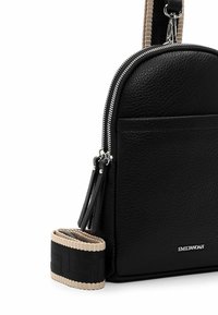 Black leather bag with textured surface, rounded shape, silver zipper, and a beige patterned shoulder strap featuring a black accent.