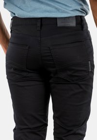Pantalons en denim noir au design ajusté. Présentent deux poches arrière et des accents de couture. Le matériau semble lisse et légèrement extensible.