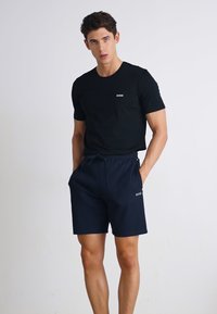 Camiseta negra de manga corta con logo en el pecho, combinada con pantalones cortos azul marino con cordones. Ambos artículos tienen una textura suave y un ajuste casual.