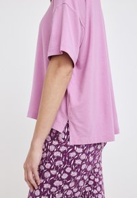 Top corto de manga corta en rosa claro con un corte relajado, que presenta una abertura lateral. Combinado con pantalones morados de estampado floral.