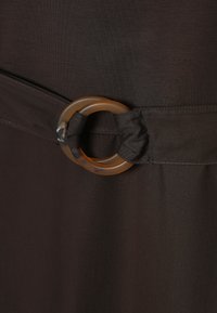 Gros plan sur une ceinture en tissu marron foncé avec une boucle circulaire translucide marron passée à travers la boucle en tissu.