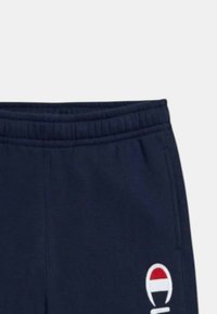 Pantaloni da tuta blu navy con vita elastica e tasche laterali, con un logo rosso e bianco sulla gamba sinistra. Materiale in cotone morbido.